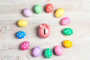 Piggy bank surrounded by Easter eggs on a light wooden background.