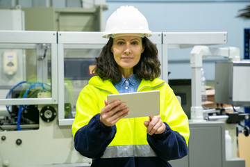 Front view of female technician with tablet looking at camera. Confident factory worker using...