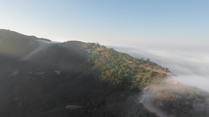 Aerial view of a canyon and a bend of the road in the morning sunshine and clouds below (Malibu Canyon, Monte Nido, California, USA)