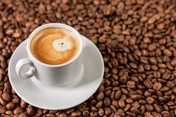 A white cup with aromatic coffee stands on scattered grains. Close-up. Space for text.
