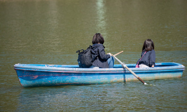 春の公園の池で手漕ぎボートを遊んでいる親子