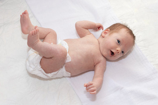 Happy baby girl lying on white sheet wearing a diaper. Cute adorable baby is 1 month old. Dry and healthy body and skin for children concept. Nursery for children.