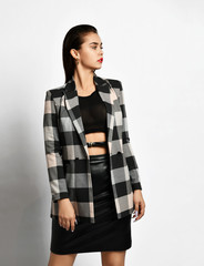 Young sexy brutal brunette woman in checkered jacket, black leather skirt and cross-belt is looking...