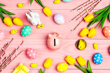 Piggy bank surrounded by eggs and Easter decoration on a pink wooden background.