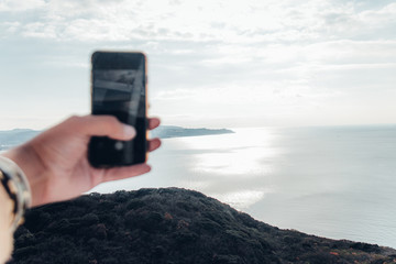 灯台で柵から手を出してスマホで写真撮影。自分探しの旅イメージ。海