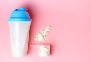 Cocktail shaker and measuring spoon with protein on pink background, copy space.