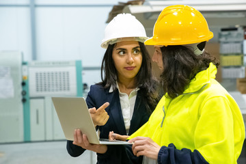 Confident women with laptop at manufacturing plant. Two female employees talking while standing at factory with laptop. Print manufacturing concept