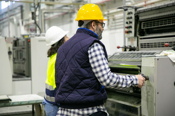 Two factory employees working with printing machine. Professional operators working at printing house. Print manufacturing concept