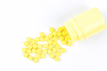 Selective focus of yellow medicine pills and tablets spilling out of a drug bottle on white background with copy space for your text..