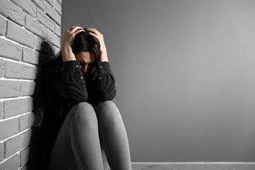 Depressed young woman near grey wall