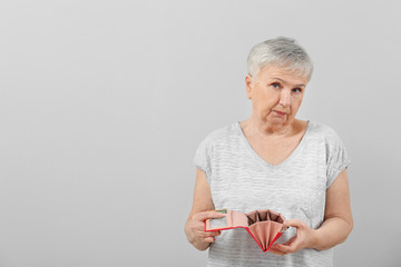 Senior woman with empty wallet on light background