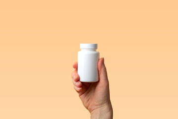 Viral disease prevention concept. Female hand holds jar with vitamins, pills, medicines or drugs on orange background. Coronavirus prevention. Safety rules during quarantine. Copy space for  text