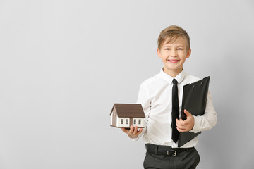 Portrait of little real estate agent with model of house on light background