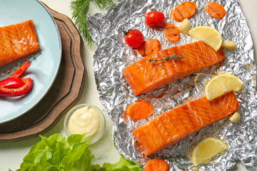 Foil with cooked salmon fillet and vegetables on table