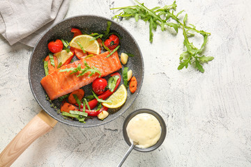 Frying pan with cooked salmon fillet and vegetables on white background