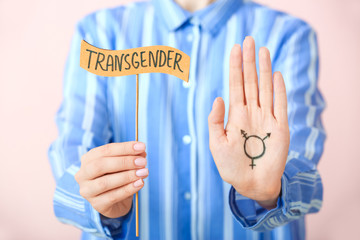 Woman holding stick with word TRANSGENDER on color background
