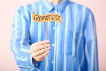Woman holding stick with word TRANSGENDER on color background