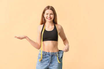 Woman in loose jeans and with weight loss pills on color background