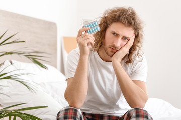 Sad man with oral erectile dysfunction medication in bedroom