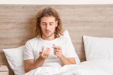 Young man with oral erectile dysfunction medication and condom in bedroom