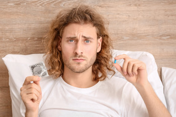 Sad man with oral erectile dysfunction medication and condom in bedroom