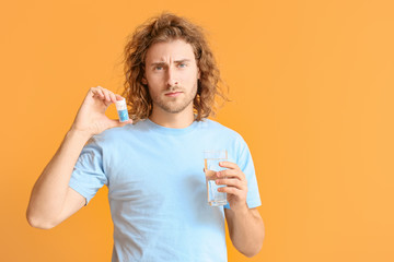 Young man with oral erectile dysfunction medication on color background