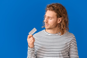 Young man with oral erectile dysfunction medication on color background