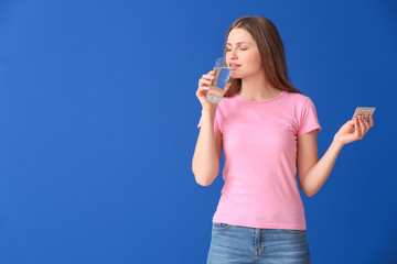 Fototapeta premium Young woman taking birth control pills on color background