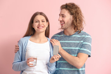 Young couple with birth control pills on color background