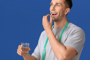 Young man taking weight loss pills on color background