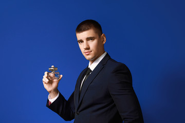 Handsome young man with bottle of perfume on color background