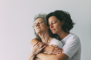 Peaceful serene adult daughter hugging senior mother. Middle aged woman with closed eyes embracing...