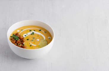 Pumpkin cream soup decorated with chickpeas, sour cream, lime, olive oil, pepper. Copy space. Isolated. Close up. Vegetarian, healthy food, diet, recipe or menu concept. Grey background. 