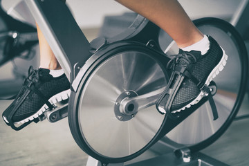Fitness machine at home woman biking on indoor stationary bike exercise indoors for cardio workout. Closeup of shoes on bicycle. - obrazy, fototapety, plakaty
