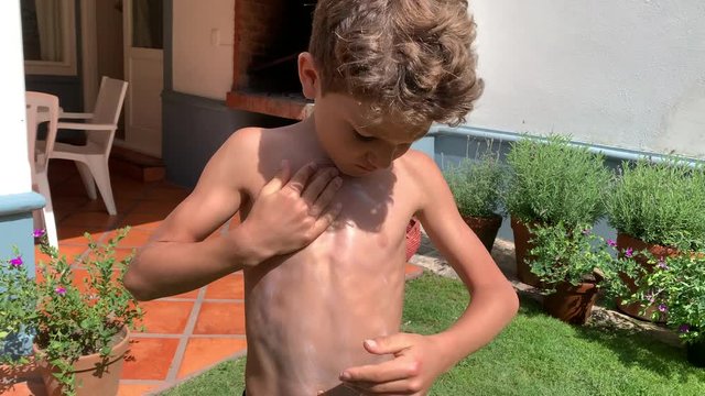 Child rubbing sunblock lotion into body chest. Young boy applying sunscreen protection