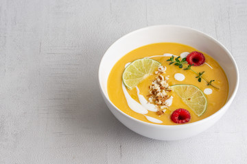 Carrot, pumpkin cream soup decorated with nuts, sour cream, lime, raspberries olive oil, pepper. Isolated. Copy space. Vegetarian, healthy food, diet, recipe or menu concept. Grey background