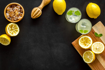 Homemade lemonade in glasses near juicer and cut lemons on black background top-down copy space