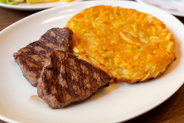 Closeup view of delicious grilled beef medallions served on table. Grilled beef steaks with spices on white plate. Grilled beef steak and fried potatoes isolated on white plate.