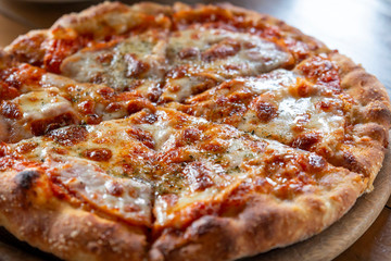 Ham and Cheese Pizza. Hot pizza slice with dripping mozzarella cheese. Pizza with cheese on board and wooden table background. Pizza slice with melting cheese. Selective focus.