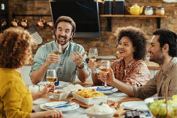 Happy friends toasting with wine while eating lunch together at dining table.