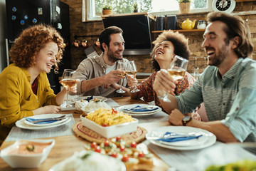 Happy young adults having fun while toasting with wine at dining table.