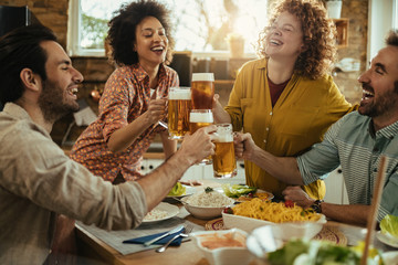 Group of happy friends having fun while toasting with beer at dining table.
