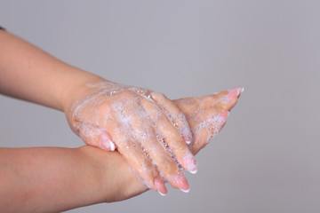 Washing female hands with soap on a gray background