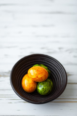 Four Easter eggs in yellow and green colors in dark brown wooden plate on white wooden background. Selective focus, Easter card. Happy Easter!