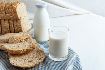 A bottle of milk and glass of milk with sliced bread on cloth indoors background for food and healthy concept. with copy space for text.