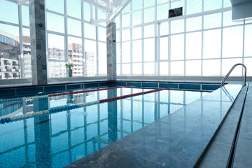 Indoor swimming pool with panoramic windows overlooking city buildings