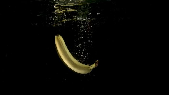 One fresh mature yellow banana falling in the clear water. Steady underwater slow motion camera shot.