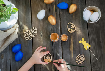 Happy Easter.Kids paints with paint balls and wooden crafts.Blue, Golden eggs on a rustic wooden background on a Sunny day.Spring holiday.DIY.Instructions. Preparing for the holiday.Flat lay
