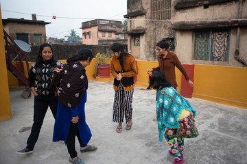 A cheerful Indian Bengali family in winter garments enjoying in a sunny winter afternoon by playing football on a rooftop. Indian lifestyle.