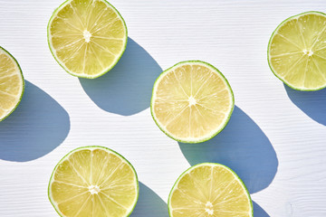 Ripe lime halves on white wooden background, close-up shot from above in harsh sunlight with long...